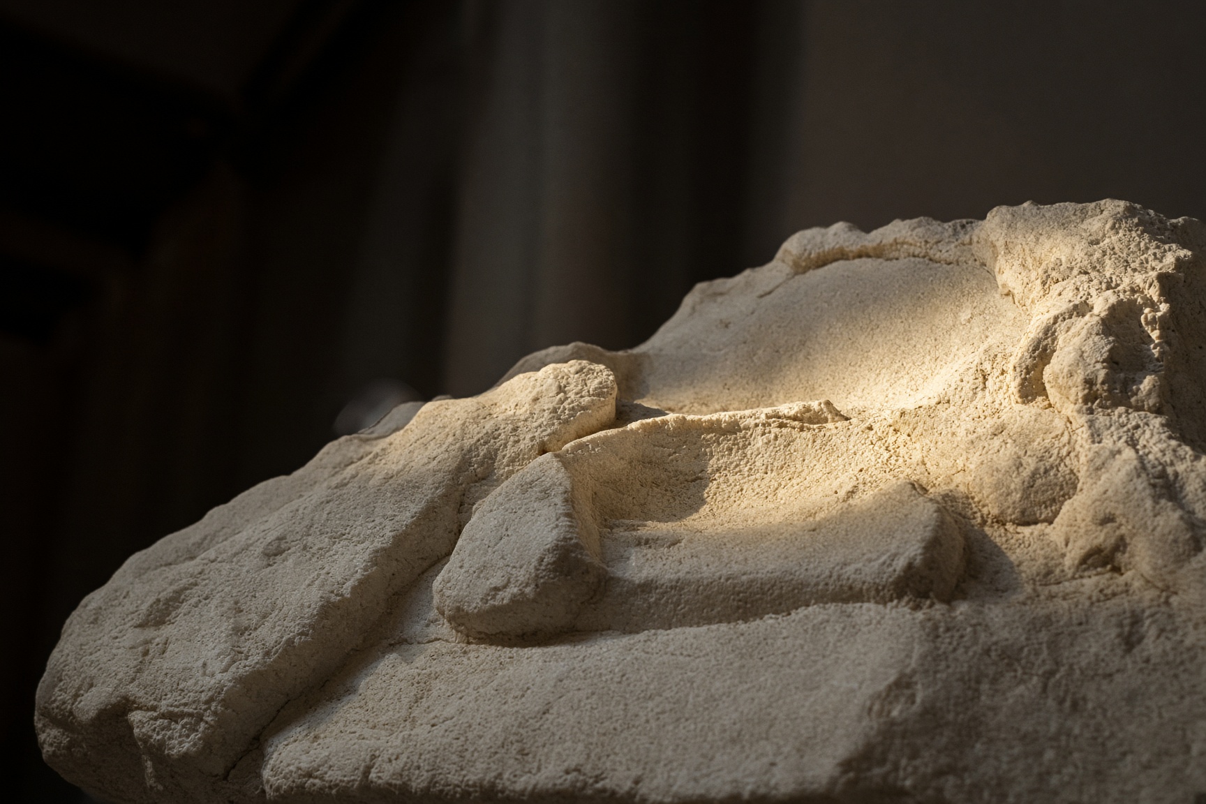 Raking museum light across a pale fragment of carved marble.