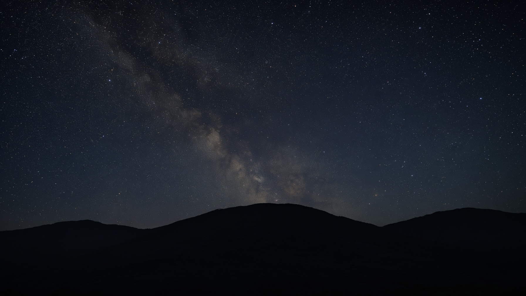 Long-exposure night sky over a dark ridge, gold dust of stars.