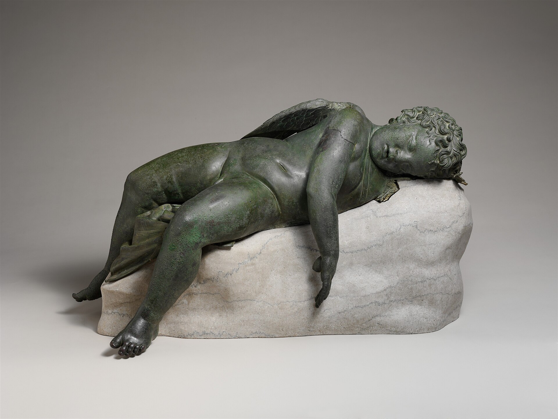 Bronze statue of a small winged Eros asleep on a rock.